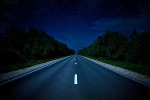 long stretch of road at night with woods on both sides