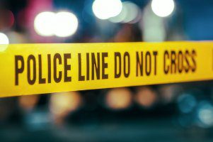image shows police tape with the blurred lights of emergency vehicles in the background